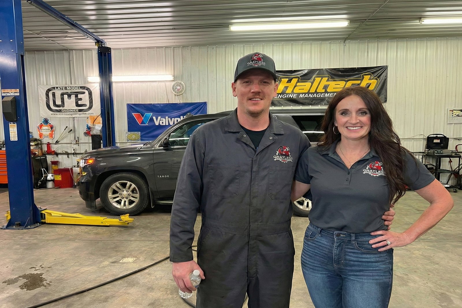 Interior of Grayless Automotive & Performance showing a silver Chevrolet Corvette on a professional Rotary lift. The clean workshop features a large American flag and organized tool stations.